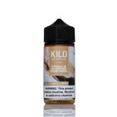 A 100ml bottle of Kilo Vanilla Almond Custard e-liquid on a white background with a reflection below. The bottle has a black cap and a label featuring brown and beige tones with vanilla and almond imagery.